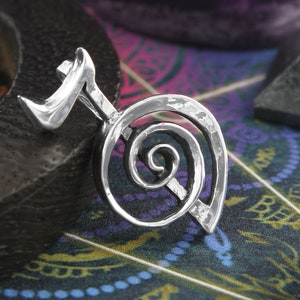 May include: Silver pendant featuring a spiral design with a small, pointed extension at the top. The pendant has a hammered texture.
