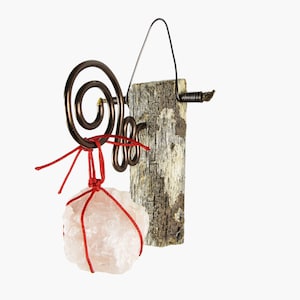 May include: A handcrafted decorative piece featuring a rough, light pink crystal suspended by red string from a copper wire spiral. The crystal hangs in front of a piece of weathered wood, with a black wire handle.
