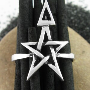 May include: A silver ring with a pentagram design. The ring is set against a background of black incense sticks.