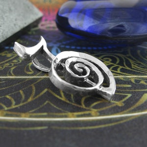 May include: A silver charm pendant in the shape of a spiral, with a smooth, polished finish. The pendant is on a dark background with a blue stone.