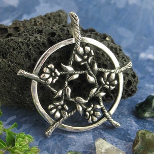 May include: A silver pendant featuring a pentagram with five stylized flowers, each with five petals, within a circle. The pendant is made of silver and has a detailed, intricate design.