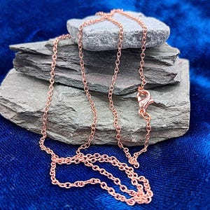 May include: A rose gold-toned metal chain necklace featuring a series of interconnected oval links. The necklace includes a lobster claw clasp mechanism for securing the ends together, showcasing a metallic finish and a delicate, lightweight link design.