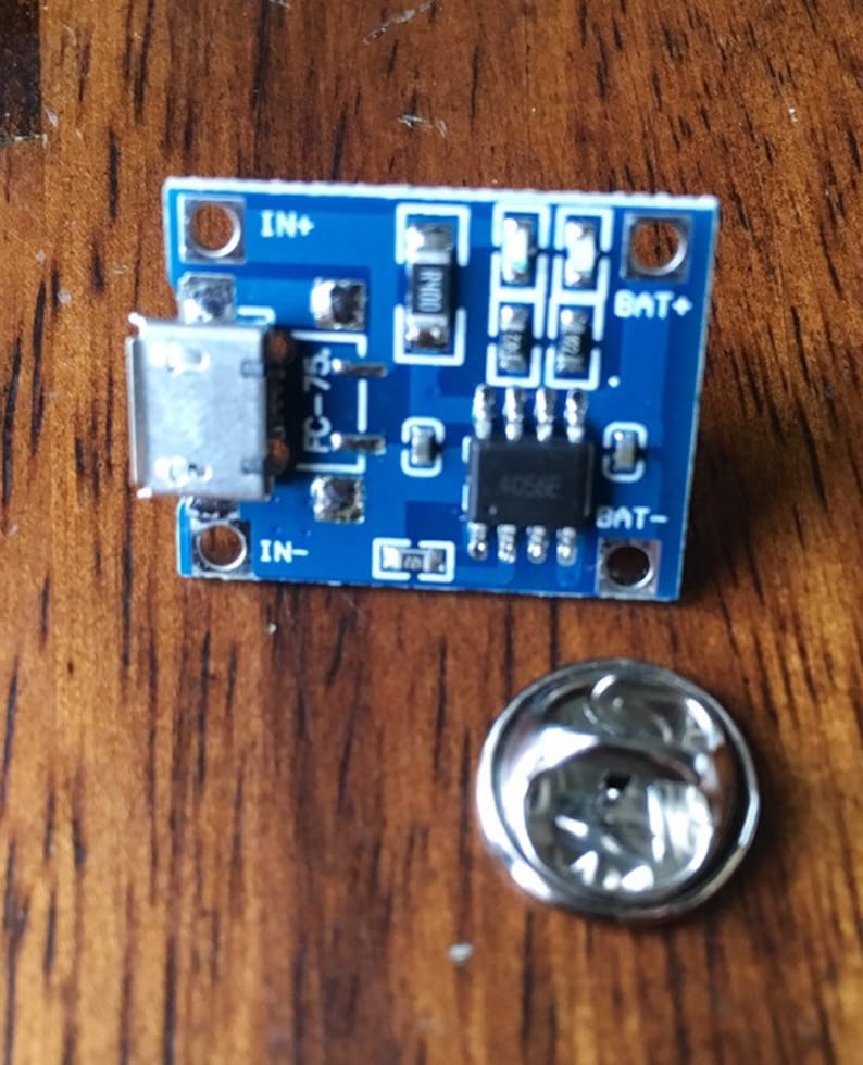 May include: A blue circuit board with a micro USB connector, labelled "IN+", "IN-", "BAT+", and "BAT-".