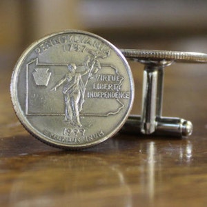 May include: Silver cufflinks featuring a 1999 Pennsylvania state quarter coin with the inscription "Virtue Liberty Independence".
