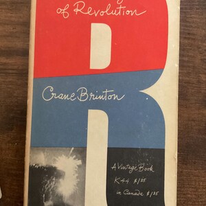 May include: Vintage book cover titled "The Anatomy of Revolution" by Crane Brinton. The cover features a large red "R" shape over a blue background. The title is in white script, with the author's name below. A black and white image is on the bottom left.