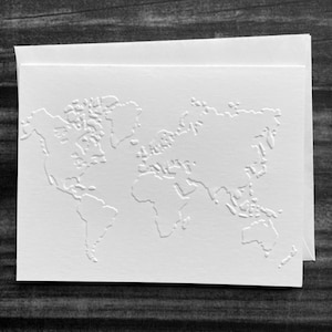 May include: A white card and envelope set featuring a detailed embossed world map design. The card's surface has a textured feel, with continents and islands raised from the paper. The set is ideal for sending travel-themed notes or invitations.