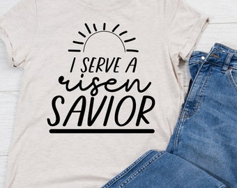 May include: A beige t-shirt with a black graphic design that reads "I serve a risen SAVIOR" with a sun graphic above the text.