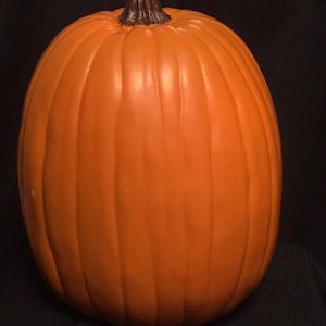 May include: A large, orange pumpkin with vertical ridges and a dark brown stem. The pumpkin is round and smooth, perfect for fall decorations or Halloween.
