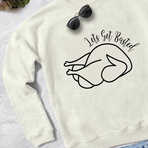 May include: White sweatshirt with a black outline of a turkey and the text "Let's Get Basted".