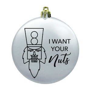 May include: A silver Christmas ornament with a black and white illustration of a nutcracker and the text "I WANT YOUR NUTS".