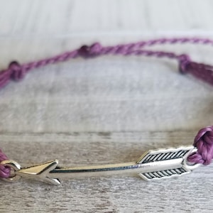 May include: A purple braided cord bracelet with a silver arrow charm.