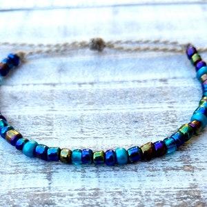 May include: A blue and iridescent beaded bracelet with a white cord closure.