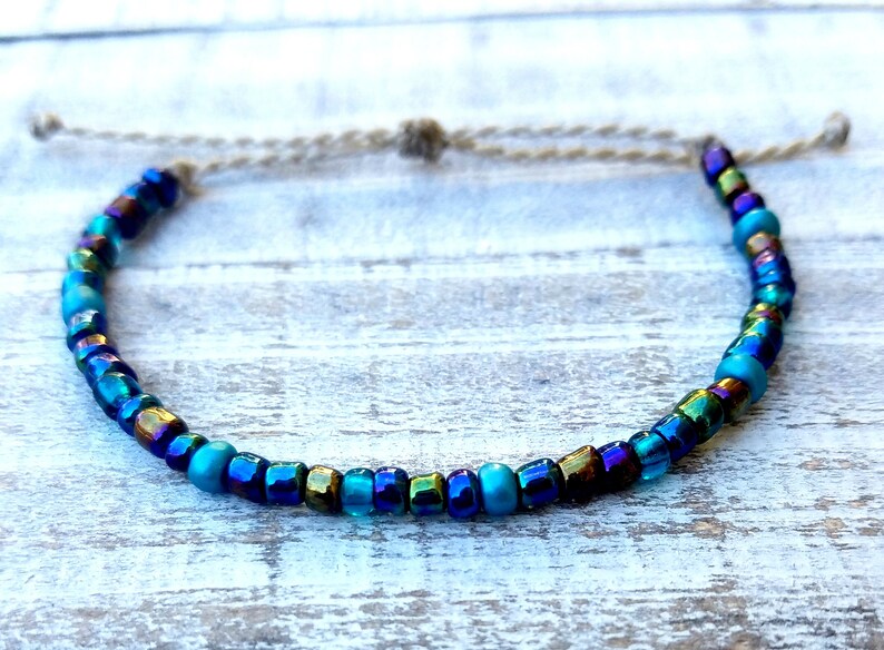May include: A blue and iridescent beaded bracelet with a white cord closure.