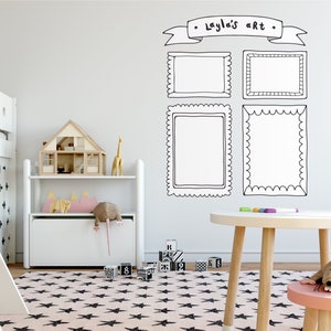 May include: A white wall with black and white doodle frames that say "Layla's Art" above them. There is a white toy shelf with a wooden dollhouse on it. There is a pink and white star rug on the floor.