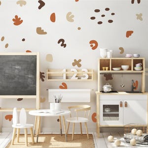 May include: A child's playroom with a chalkboard easel, a small table and chairs, and a wooden play kitchen. The walls are decorated with abstract shapes in brown and tan colors. The room has a neutral color palette.