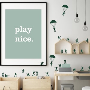 Può includere: Una stampa incorniciata con le parole "play nice" in bianco su sfondo verde salvia. La parete è decorata con soldatini e paracadutisti verdi. Mensole in legno e un tavolino con contenitori completano la scena giocosa.