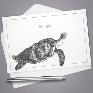 May include: A white rectangular greeting card featuring a detailed black and white ink illustration of a sea turtle swimming. The text SHELL YEAH! is printed in black above the turtle. A silver metal pen rests horizontally below the card.