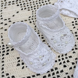 Puede incluir: Un par de zapatos de bebé de ganchillo blanco con adornos de perlas. Los zapatos tienen un delicado diseño de encaje y son perfectos para una ocasión especial.