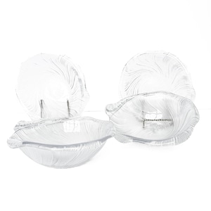 Può includere: Quattro ciotole e piatti di vetro trasparente con un design a conchiglia. Le ciotole e i piatti hanno un motivo a vortice strutturato. Le ciotole sono di forma ovale e i piatti sono rotondi. Gli articoli sono su sfondo bianco.