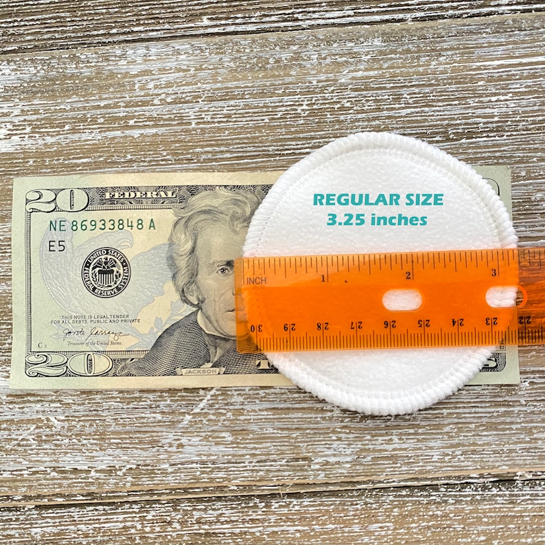 May include: A white cotton round makeup remover pad measuring 3.25 inches in diameter, next to a twenty dollar bill and a ruler.