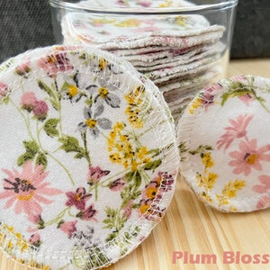 May include: A close-up of a stack of reusable cotton rounds with a floral print. The rounds are white with pink, yellow, and gray flowers. The text "Plum Blossom" is visible at the bottom of the image.