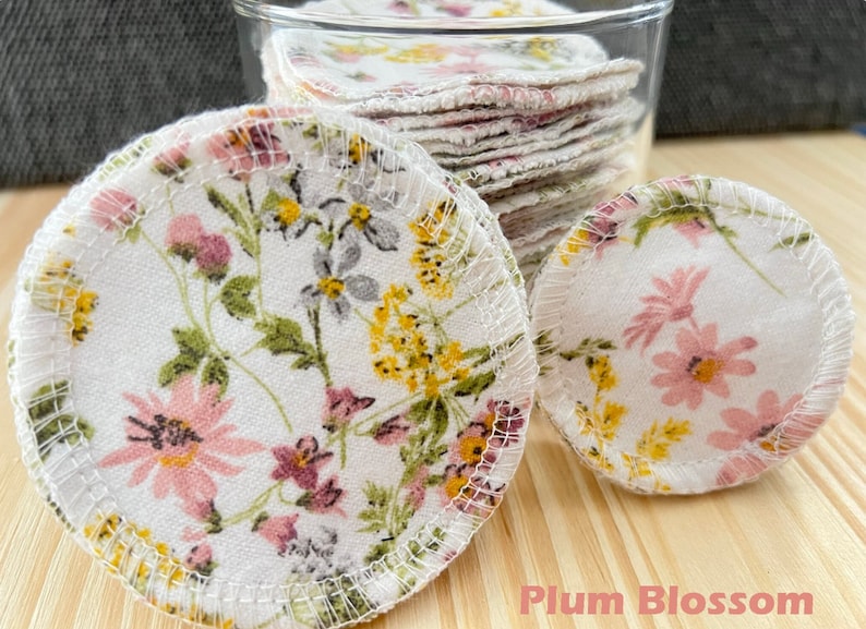 May include: A close-up of a stack of reusable cotton rounds with a floral print. The rounds are white with pink, yellow, and gray flowers. The text "Plum Blossom" is visible at the bottom of the image.