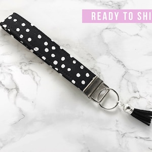 May include: Black and white polka dot wristlet keychain with a silver-tone metal clasp and key ring. The keychain has a black tassel and the text "READY TO SHIP" in a pink banner.