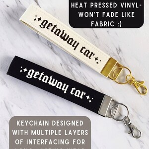 May include: Two keychains, one cream and one black, each with the text "getaway car" in a gothic font. The cream keychain has a gold clasp, while the black one has a silver clasp. Text on the image states "Original design made with durable heat pressed vinyl - won't fade like fabric".