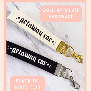 May include: Two wrist keychains with the text "getaway car" in a gothic font. One keychain is cream-colored with gold hardware, the other is black with silver hardware. The image text reads "Choose between: Gold or Silver Hardware" and "Black or White Text."