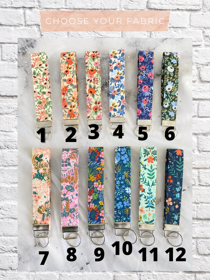 May include: Twelve fabric key fobs with floral patterns in various colors, including pink, orange, blue, and green. Each fob has a silver-colored metal ring and a loop for attaching keys. The text "CHOOSE YOUR FABRIC" is at the top.