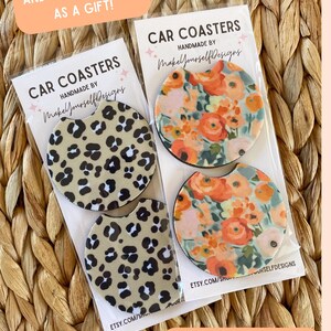 May include: Two sets of car coasters are displayed, each packaged in clear plastic. One set features a leopard print design, while the other showcases a floral pattern with orange and pink flowers. Text on the packaging reads "Car Coasters" and "Handmade by MakeYourselfDesigns."