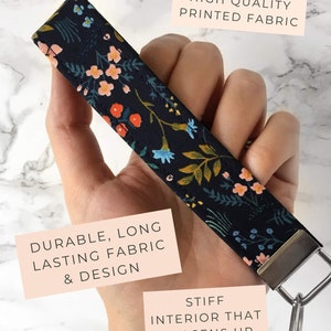 May include: A floral patterned wristlet key fob with a dark background and colorful flowers. The key fob has a metal clasp and key ring. The text on the image says "High Quality Printed Fabric" and "Durable, Long Lasting Fabric & Design."