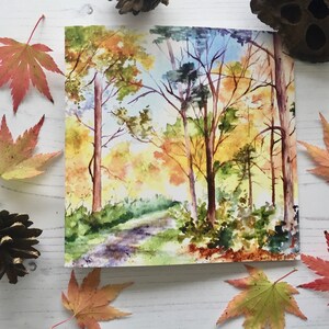 May include: Watercolor painting of a forest path with trees in autumn colors. The trees are mostly yellow and orange, with some green leaves still remaining. The path is winding through the forest, and there is a bright blue sky in the background.
