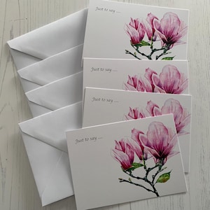 May include: A collection of white greeting cards and envelopes. Each card displays a watercolour illustration of pink magnolia flowers and the text "Just to say...."