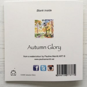 May include: A greeting card featuring a watercolor painting of an autumn forest scene with a path leading through the trees. The card has the text "Autumn Glory" and "from a watercolor by Pauline Merritt ART &copy; www.paulinemerritt.net" printed on the front. The back of the card has a barcode and social media icons.