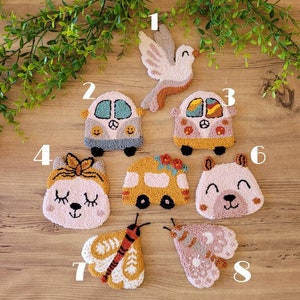 Op de afbeelding: Een verzameling van acht punch needle geborduurde patches met diverse ontwerpen: een duif, twee campers, een kat met een strik, een gele bus, een berengezicht en twee motten. Elke patch is genummerd van &eacute;&eacute;n tot acht met gedetailleerde textuur van garen.