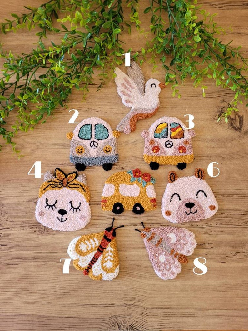Op de afbeelding: Een verzameling van acht punch needle geborduurde patches met diverse ontwerpen: een duif, twee campers, een kat met een strik, een gele bus, een berengezicht en twee motten. Elke patch is genummerd van &eacute;&eacute;n tot acht met gedetailleerde textuur van garen.