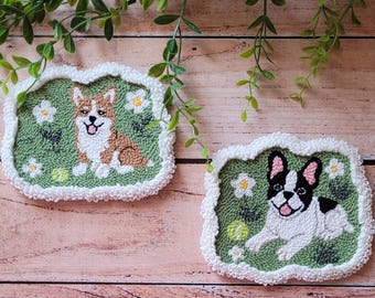 May include: Two rectangular punch needle coasters with white fluffy borders. One features a brown and white Corgi, the other a black and white French Bulldog. Both are set against a green background with white flowers and a yellow tennis ball.