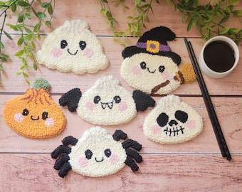 May include: A collection of six tufted textile coasters featuring Halloween-themed characters including a white ghost, a pumpkin, a bat, a spider, a skull, and a witch-hatted figure, all with embroidered facial details and pink blush accents.