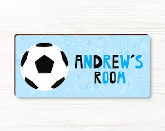 Puede incluir: Un letrero rectangular con un diseño de balón de fútbol y el texto "ANDREW'S ROOM". El letrero tiene un fondo azul claro con un patrón moteado y un borde marrón oscuro. El balón de fútbol es blanco y negro.