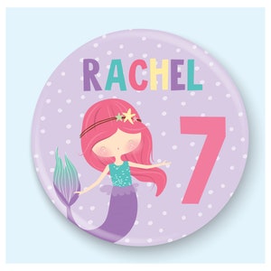 Puede incluir: Un círculo morado con lunares blancos con el nombre "RACHEL" en letras arcoíris y un número 7 rosa. Una sirena de dibujos animados con cabello rosa, cola turquesa y una concha morada está en el centro del círculo.
