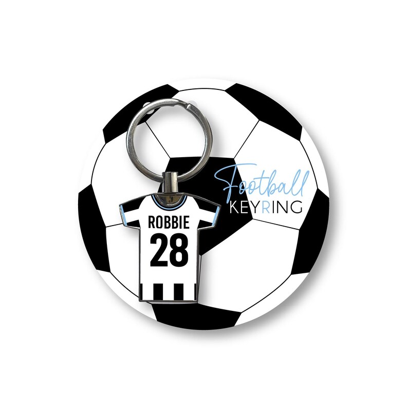 K&ouml;nnte beinhalten: Ein Fu&szlig;ball-Schl&uuml;sselanh&auml;nger mit einem schwarz-wei&szlig;en Fu&szlig;ball-Design. Der Anh&auml;nger hat einen Trikot-f&ouml;rmigen Charm mit dem Namen "Robbie" und der Nummer "28". Der Text "Football KEYRING" ist ebenfalls zu sehen.