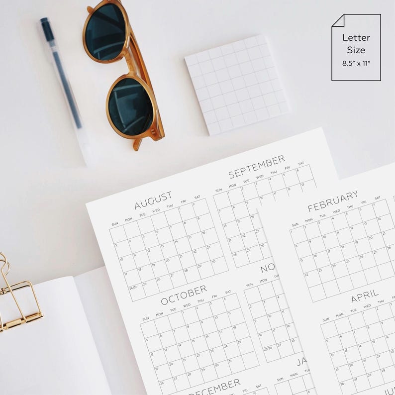 May include: A white paper calendar with black text showing the months of August, September, October, November, February, and April. The calendar is letter size, measuring 8.5 inches by 11 inches, accompanied by a black pen, sunglasses, and a gold clip.