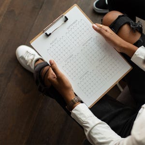 May include: A wooden clipboard holding a white paper sheet printed with a six-month calendar grid. The calendar displays the months of August, September, October, November, December, and January, each organized into a grid of numbered days.