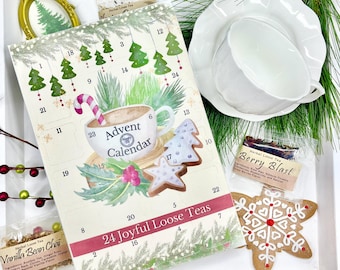 May include: A Christmas-themed gift set featuring an Advent calendar with 24 tea selections. The set includes a white teacup and saucer, gingerbread cookies, and loose-leaf tea packets. The calendar has a cup of tea illustration.