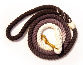 May include: A black, gray, and white ombre cotton rope dog leash with a gold metal clasp.