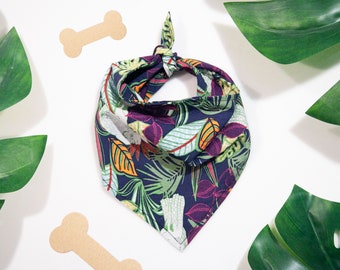 May include: A blue bandana with a tropical leaf print in shades of green, orange, and purple. The bandana is tied in a knot at the top and has a white border.