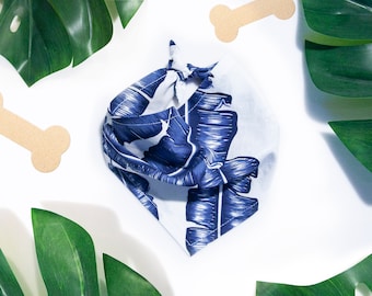 May include: A white bandana with a blue and white tropical leaf print. The bandana is tied in a knot and is on a white background.