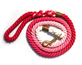 May include: A red, pink, and white ombre cotton rope dog leash with a gold metal clasp.