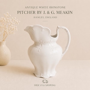 May include: An antique white ironstone pitcher by J. & G. Meakin, Hanley, England. The ceramic vessel features a scalloped rim, a curved handle, and embossed floral detailing around the neck and base. The text reads: ANTIQUE WHITE IRONSTONE PITCHER BY J. & G. MEAKIN HANLEY, ENGLAND.
